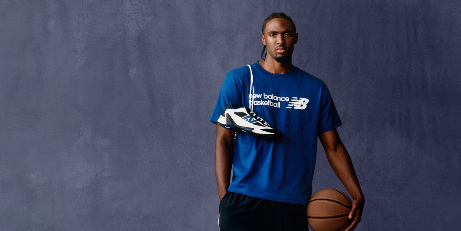A person wearing a blue New Balance Basketball T‑shirt poses against a plain backdrop. 